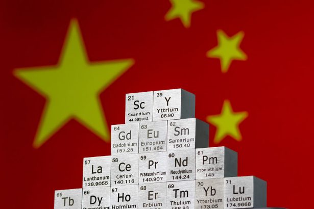 In this photo illustration, metal cubes representing rare earth elements including Scandium (Sc), Yttrium (Y), Neodymium (Nd), Lanthanum (La), and others are stacked in a stepped formation in front of the national flag of China