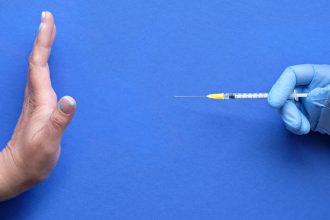 Vaccine refusal concept. Medic hand in glove with syringe. Hand refusing vaccination from measles or Covid-19. Anti-vaccination concept image with refusal gesture.