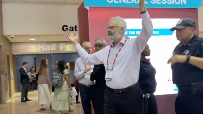 Police escort Dr. Steven Kuhn out of a medical conference in New Orleans for handling out copies