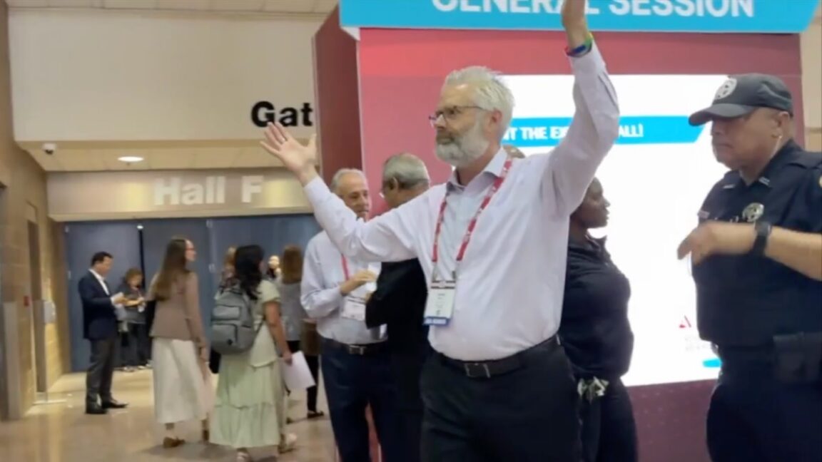 Police escort Dr. Steven Kuhn out of a medical conference in New Orleans for handling out copies